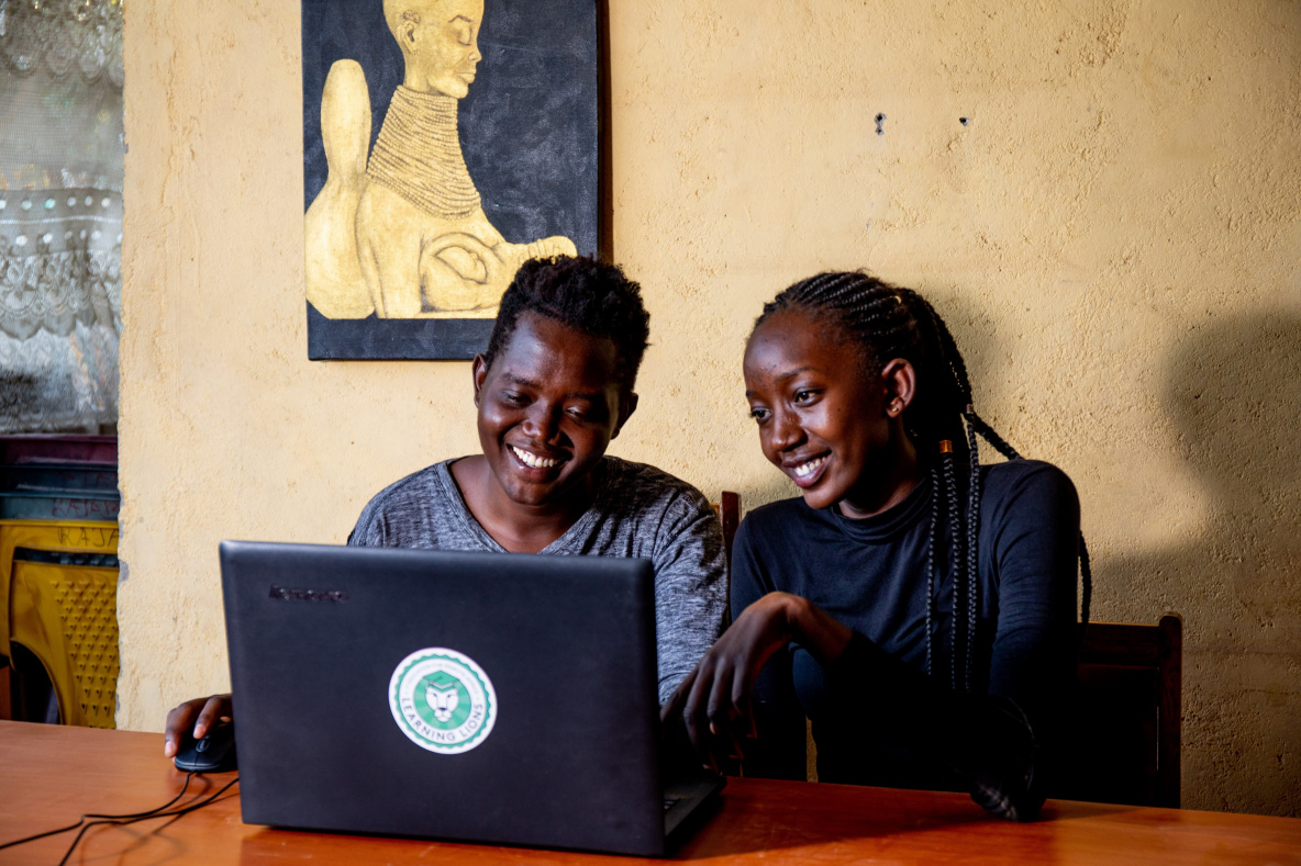 2 Kenyan people smiling while looking at a laptop screen