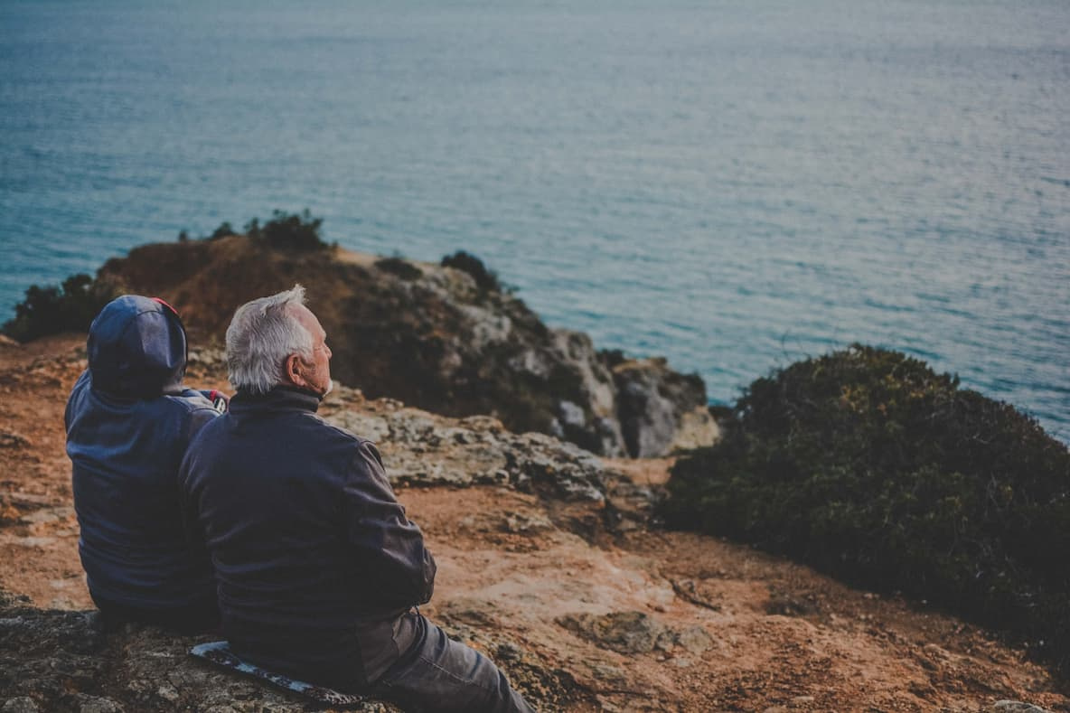 Elderly couple sitting on a cliff overseeing the sea