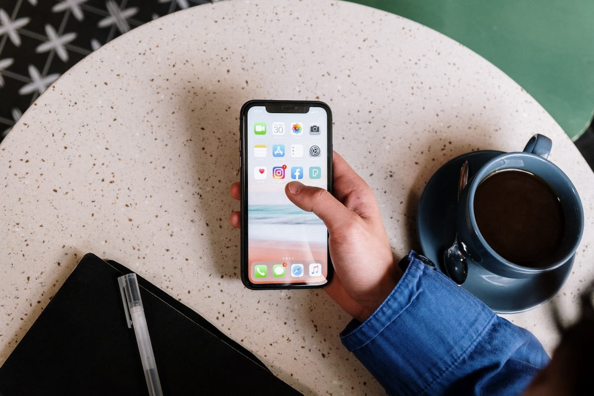 Image in the point of view of a user holding a mobile phone over a table next to a cup of coffee