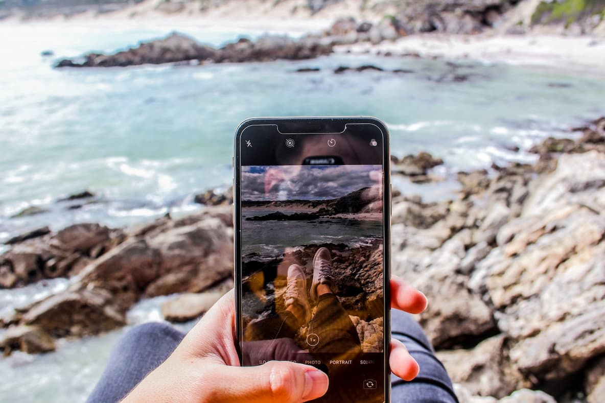 Image in the point of view of a user taking a picture of their feet on some rocks near the s