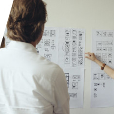 Man looking at user interface sketches while someone outside the picture points at them