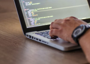 Hand on a laptop displaying a text editor with CSS code